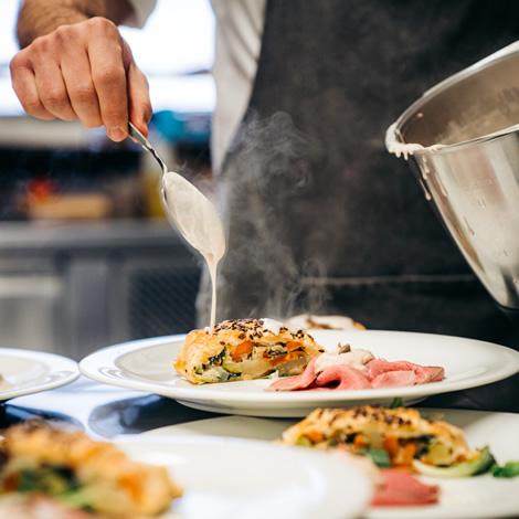 Chef serves hot dish with creamy sauce, gourmet and inviting atmosphere.