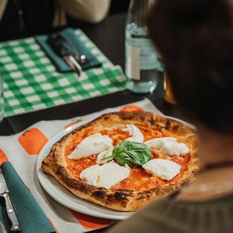 Warm margherita pizza with mozzarella and basil, convivial atmosphere in a pizzeria.