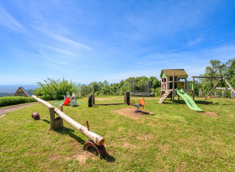 Sunny playground with swings, slide, and panoramic view over green hills.