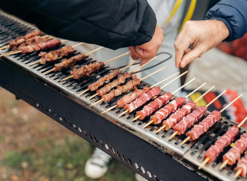 Grilled meat skewers outdoors, skilled hands turning them carefully.