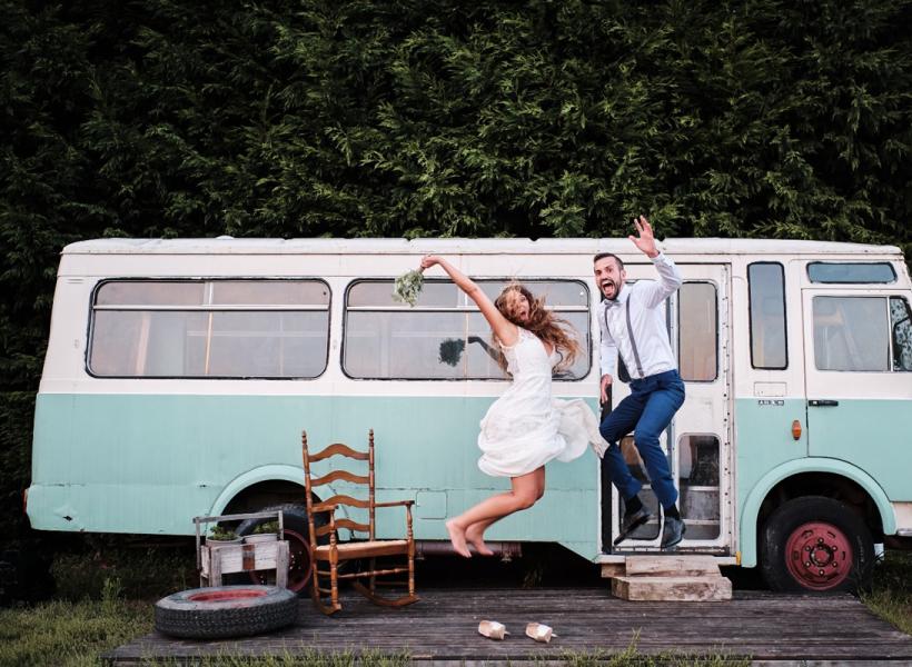 Joyful couple jumps in front of vintage bus, evoking happiness and freedom.