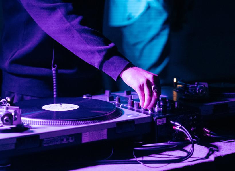 A DJ mixing vinyls, purple lights create a vibrant and dynamic atmosphere.